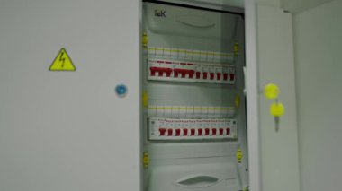 Güvenlik levhası, manivela ve uyarı etiketlerinin görüldüğü endüstriyel bir ortamda elektrik kabinesini aç. Elektrik güvenliği ve endüstriyel ekipmanlara odaklan. Çoklu Kollu Elektrik Kabinesi