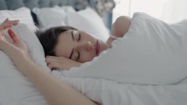 Beyaz bir battaniyeye sarılı rahat bir yatakta uyuyan genç bir kadın huzur ve rahatlama hissi yaratıyor. Dinlenme ve rahatlama kavramları için mükemmel bir görüntü. Genç Kadın Uyuyor