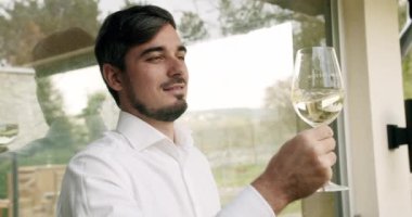 Şarap tadımı yapan adam. Camların dönüşü şarabın yüzeyini dalgalandırıyor ve uzun cam duvarlar boyunca uzanıyor. Sommelier beyaz şarap bardağını sallıyor ve tadına bakıyor..