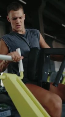 Modern bir spor salonunda kürek çeken odaklanmış bir adam. Spora adanmış bir ortamda spor eğitimi, egzersiz ve dayanıklılık. Azimli Adam Jimnastik Salonunda Dikey İdman Yapıyor