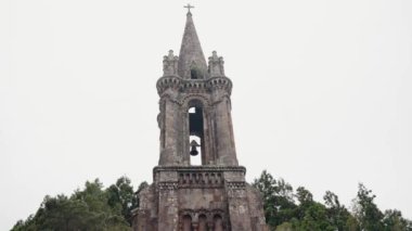Portekiz 'deki Antik Taş Çan Kulesi yemyeşil ortamda. Görkemli antik bir taş çan kulesi, Portekiz 'deki yemyeşil çimlerin ortasında duruyor, çarpıcı tarihi bir mimari sergiliyor..