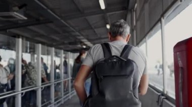 Sırt çantalı bir adam kalabalık bir otobüs durağında yürüyor ve tek başına seyahat etmenin ve şehir hayatının özünü yakalıyor. Orta yaşlı adam işlek bir otobüs durağında tek başına seyahat ediyor.