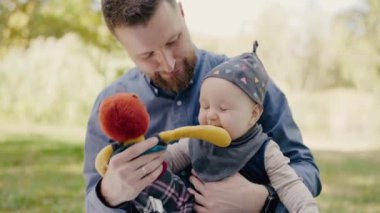 Baba ve Oğlan dışarıda eğlenceli bir anın tadını çıkarıyorlar. Genç bir baba, elinde oyuncakla gülümseyen küçük oğluyla doğal bir park zeminine karşı neşeli bir anı paylaşır..