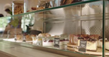 Modern bir kafede cam bir kutuda sergilenen cazip taze tatlıları keşfedin. Cheesecakelerden kurabiyelere kadar her öğe baştan çıkarıcı bir şekilde fiyat etiketleriyle sunuluyor.