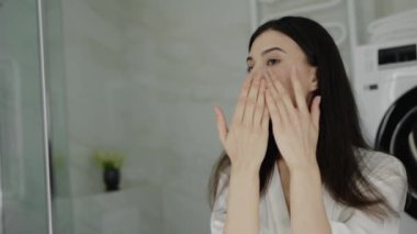 Genç bir kadın, modern ve temiz bir banyoda cilt bakım ürününü yüzüne uyguluyor. Görüntü kişisel bakım ve günlük güzellik rutinlerini vurguluyor. Modern Tuvalette Cilt Ürünü Uygulayan Kadın