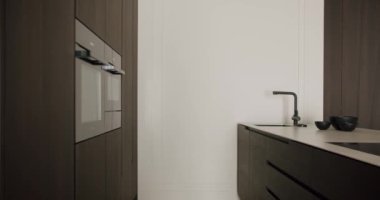 Karanlık ahşap dolaplar, entegre aletler ve parlak bir tasarım içeren çağdaş minimalist mutfak. Modern ev fikirleri ve iç dekorasyon için mükemmel. Modern Minimalist Mutfak