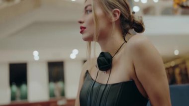 Kırmızı dudaklı ve şık giysili şık bir kadın modern ve aydınlık bir çevrede oturuyor. Arka planda zarif bir dekor ve Bokeh ışıklandırması var. Şık Genç Güzel Kadın