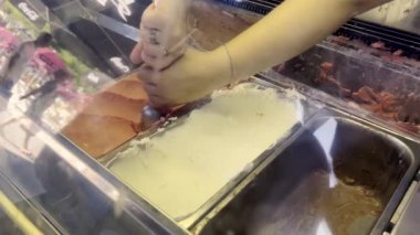 Bir el dondurma dükkanının vitrinindeki farklı dondurma çeşitlerini topluyor. Sahne, arka planda insanların olduğu canlı bir yaz gününü çağrıştırıyor. Gelateria 'da dondurma.