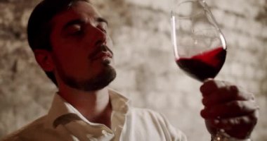 Erkek şarap üreticisi bir tat alıyor ve taze kırmızı şarabı kontrol ediyor. Fabrikada ya da depoda şarap içen bir adam. Güzel giyimli Sommelier bir bardak kırmızı şarabı kontrol edip içiyor. Şarap yapımı konsepti.