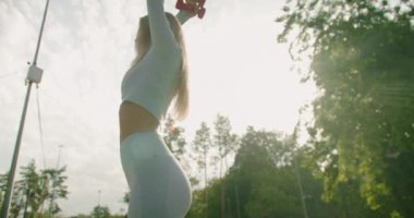 Mavi moda aktif giyimli genç bir kadın kolları için spor yapıyor ve dambılları kaldırıyor. Mavi aktif giysili sporcu kız sabah dışarıda kulaklıkla müzik dinliyor ve egzersiz yapıyor..