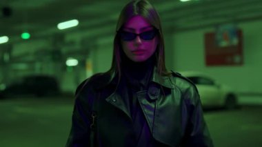 Deri ceketli kadın park halindeki arabalara karşı büyüleyici bir görsel birliktelik yarattı. Şık bir kız. Genç, lüks, seksi bir kadın karanlık arka planda kameraya bakıyor..