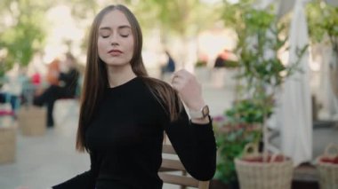 Uzun saçlı ve doğal makyajlı düşünceli bir kadının, sakin bir ifadeyle doğrudan kameraya bakan yakın plan portresi. Ellerini nazikçe çenesinin altında dinlendiriyor..