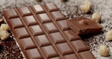 Sütlü çikolata ve fındıklı bir parça, kakao tozu ve fındıkla çevrili. Bu cezbedici görüntü hoşgörü ve tatlı ikramları göstermek için mükemmeldir..