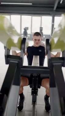 Genç adam yoğun bir şekilde spor salonunda kürek çekme makinesinde çalışıyor. Modern bir spor salonunda kürek çeken genç bir erkek sporcu azim ve kondisyon gösterisi yapıyor. Dikey video