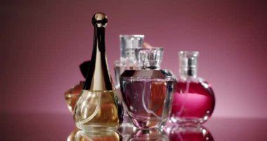 Pembe arka planlı cam bir yüzeyde sergilenen zarif parfüm şişeleri koleksiyonu. Parfümlerin çeşitliliği lüks ve sofistike, güzellik ve moda temaları için ideal.