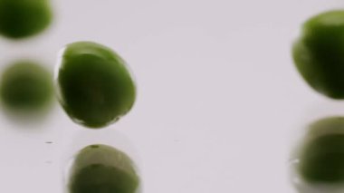Many ripe green peas rolling on a reflective surface on an isolated white background. Close up Fresh green peas. Fresh green pea on white background filmed in studio.