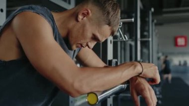 Kolsuz gömlek giyen genç bir adam spor salonunda çalışırken yoğun bir şekilde odaklanmış. Kararlılık ve zindeliğin özünü yakalamak. Spor salonunda kolsuz gömlekle spor yapan odaklı adam.