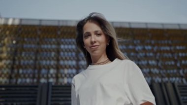 Beyaz tişörtlü zarif bir genç kadın şehir ortamında güneşli bir günün tadını çıkarıyor, rahat ve memnun görünüyor. Şehir sokaklarında poz veren günlük kıyafetlerle şık genç kadın modeller.