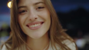 Neşeli genç bir kadının yakın plan görüntüsü. Onun yumuşak gülümsemesi ve bulanık şehir gece ışıkları sıcak ve neşeli bir ruh halini çağrıştırıyor. Şehir Işıklarıyla Gülümseyen Genç Bir Kadının Yakın Çekim Portresi