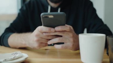 Kafede akıllı telefon kullanan, kahve fincanı ve peçeteli bir adamın yakın çekimi. Cafe 'de Akıllı Telefon Kullanan Adam, Mesaj Yazıyor, Yakın Görünüm, Kapalı Alan