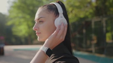 Genç bir kadın, dışarıda rahatlama ve bağlantıyı vurgulayarak, kulaklıklarıyla müzikten keyif alırken resmediliyor. Açık havada kulaklıkla müzikten hoşlanan genç bir kadın.
