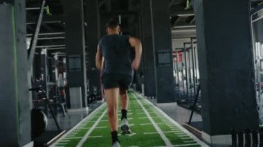 Spor salonunda spor yapan bir adamın spor salonundaki suni çim pistinde spor aletleriyle çevrili görüntüsü. Güç ve dayanıklılık üzerine yoğun çalışma oturumu.