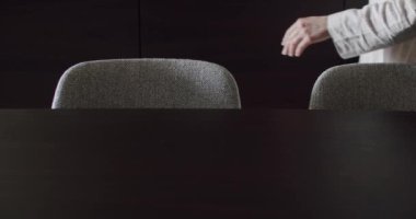 Loş bir odada gri bir sandalyenin arkasında oturmaya hazırlanan bir kişi görülüyor. Görüntü sakin ve sakin bir anı yakalar. Loş Aydınlatma Odasında bir sandalyenin yanında oturan, Oturmaya Hazır