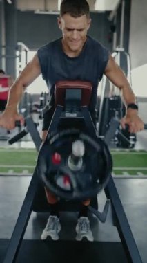 Modern bir spor salonunda spor aletleri üzerinde çalışan odaklanmış bir adam. Zindelik, güç ve kararlılık kavramı. Modern Spor Salonunda Egzersiz Aletleri Üzerinde Çalışan Kararlı Adam. Dikey