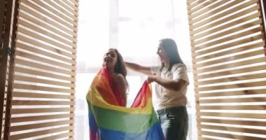 Sarılın, gülümseyin ve bayrak sallayın. Sevgilerle, LGBTQI. Lezbiyen çiftin aşk ve portresi. LGBT hakları, lezbiyen ailesi. Sevgi ve desteği paylaşan iki kadın el ele tutuşuyor.
