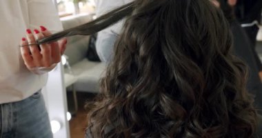 Female hairdresser making haircut to young client using curling iron in beauty studio. Handheld view of hairstylist creating trendy hairstyle. creating hairstyles hairdresser at salon. indoor shot