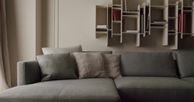 Yastıklı ve minimalist duvarlı kitaplıklarla dolu rahat gri bir kanepenin olduğu çağdaş oturma odası. Modern ev estetiği için mükemmel. Tarz sahibi Gri Koltuklu Modern Oturma Odası