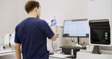 Man working in clinic laboratory. Handheld shot of male medical specialist in uniform preparing samples and using analyzing machine during work in lab of modern hospital.