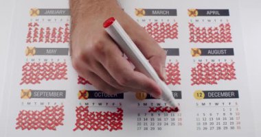 Takvimde izin günlerini kırmızı kalemle işaretleyen bir el resmi. Zamanın ve planlamanın geçtiğini gösteriyor. Takvimdeki El İşaretleme Günleri Kırmızı İşaretli Tarihleri Çizer