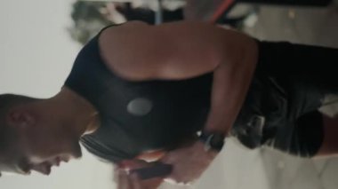 Açık havada egzersiz yapmak için direnç bantları kullanan odaklanmış erkek sporcu, doğal ışık altında güç ve zindelik gösteriyor. Atletik Adam dışarıda direniş gruplarıyla antrenman yapıyor. Dikey video.