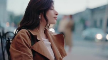 Kahverengi saçlı, şık bir ceket giyen zarif bir genç bayan, açık havada kendine güvenen bir ifadeyle oturuyor. Akşam arkaplanı. Zarif Paltolu Kahverengi Saçlı Zarif Kadın Açık havada