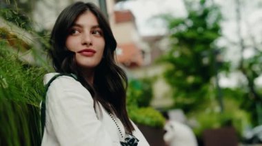 Açık havada oturan, şehir hayatını doğayla harmanlayan düşünceli ve rahat görünen genç bir kadının portresi. Doğayla iç içe olan şehir ortamında dinlenen genç kadın.