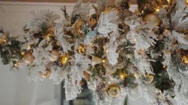 Yeni yıl tatili için hazırlık. Karlı dalları, altın topları ve parlak çelenkleri olan bir Noel ağacı. Yeni yıl süslemeli fidan ağacı. Noel arifesi kavramı. Dikey video.