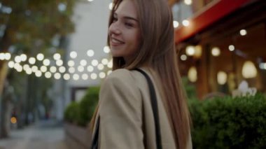 Geceleri parıldayan ışıklar ve canlı bir atmosferle çevrili bir şehirde duran gülümseyen genç bir kadın. Kentsel Ayar 'da Akşam Işıklarından Hoşlanan Genç Kadın