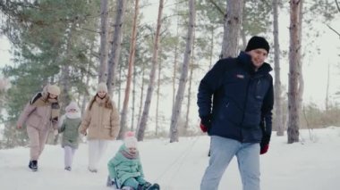 Neşeli bir aile, karlı bir kış gününün tadını çıkarıyor. Karlı bir ormanda yürüyen ve oynayan iki yetişkin ve üç çocuk, sıcaklık ve neşe çağrıştırıyor. Aile Kar ve Eğlenceyle Dışarıda Kış Gününün tadını çıkarıyor