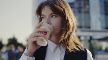 Güneşli bir günde modern şehir manzarasına sahip, açık havada kahve yudumlayan genç profesyonel bir kadın. Genç İş Kadını Kentsel Ayarlarda Kahve Molası Veriyor