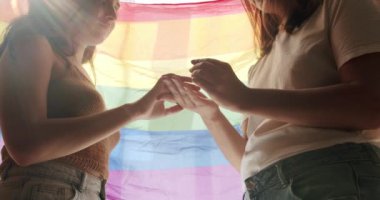 Kız sevgilisinin eline nişan yüzüğünü takıyordu, Lgbt bayrağında romantik bir kutlamanın tadını çıkarıyordu. Mutlu lezbiyen çift. Lezbiyen aile. Sevgi ve desteği paylaşan iki kadın el ele tutuşuyor.