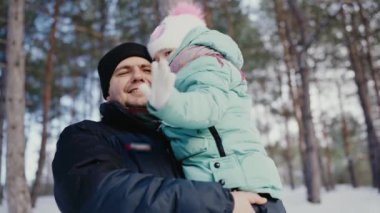 Karlı bir kış ormanında birbirlerine neşeyle gülümseyen bir baba genç kızını kollarına alır. Mutlu Baba ve Kız Karlı Ormanda.