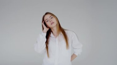 Klasik beyaz gömlek giyen, uzun düz sarı saçlı genç bir kadının portresi. Yumuşak, kendinden emin bir gülümseme sergiliyor, dostluk ve profesyonellik hissi yayıyor..