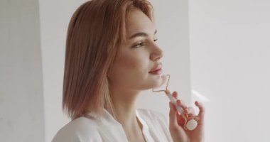 Mükemmel, pürüzsüz, sağlıklı cilde sahip güzel bir kadın yeşil yüz silindiri kullanarak masaj yaptırıyor. Evde bakım kavramı. Yüz bakımı ve güzellik ayinleri. Evde güzellik tedavisi..