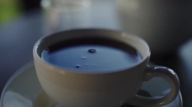 Buharı tüten bir çay fincanının yakın plan görüntüsü. Arka planda yumuşak odaklı çaydanlık, sakin bir ortamda yakalanmış. Sıcak bir ortamda Buharlı Çay Fincanının Yakın Çekimi