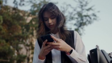 Genç profesyonel kadın, şehirde dışarıda dururken akıllı telefonunu kullanarak mesajlaşmaya odaklanmış. Modern, bağlı yaşam tarzı. Genç Profesyonel Kadın Şehirdeki Akıllı Telefonla Mesajlaşıyor