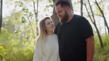 Güneşli ağaçların arasında sevgi ve mutluluk dolu bir anı paylaşan bir çifti canlandıran yürek ısıtan bir görüntü. Sevgili çift Güneş Işığı Ormanında Romantik Yürüyüşün keyfini çıkarın