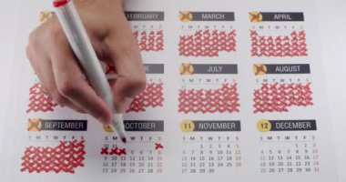 Bir takvimde günleri karalamak için kırmızı işaret kullanan bir elin yakın plan çekimi, zaman yönetimini, geri sayımı veya yıl sonunu sembolize ediyor. Aralık ayına kadar Kırmızı İşaretli Takvimdeki El İşaretleme Günleri