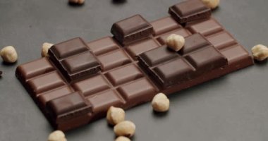 Koyu arkaplanda fındıklarla çevrili lezzetli bir çikolata parçasının yakın çekimi. Fındıklı ve koyu fındıklı lezzetli çikolata.