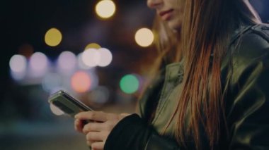 Modern teknolojiler kullanır. Çevrimiçi alışveriş ve şehir merkezinde telefonla mesajlaşan bir kadın. Şehirde dikilirken telefonu elinde tutan ve kullanan bir kadının fotoğrafı. Çevrimiçi iletişim.